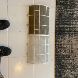 Porównanie: górna część filtra klimatyzacji silnie zabrudzona kurzem i pyłem, dolna część filtra jest czysta, po czyszczeniu, obok widoczne robocze buty i narzędzia.