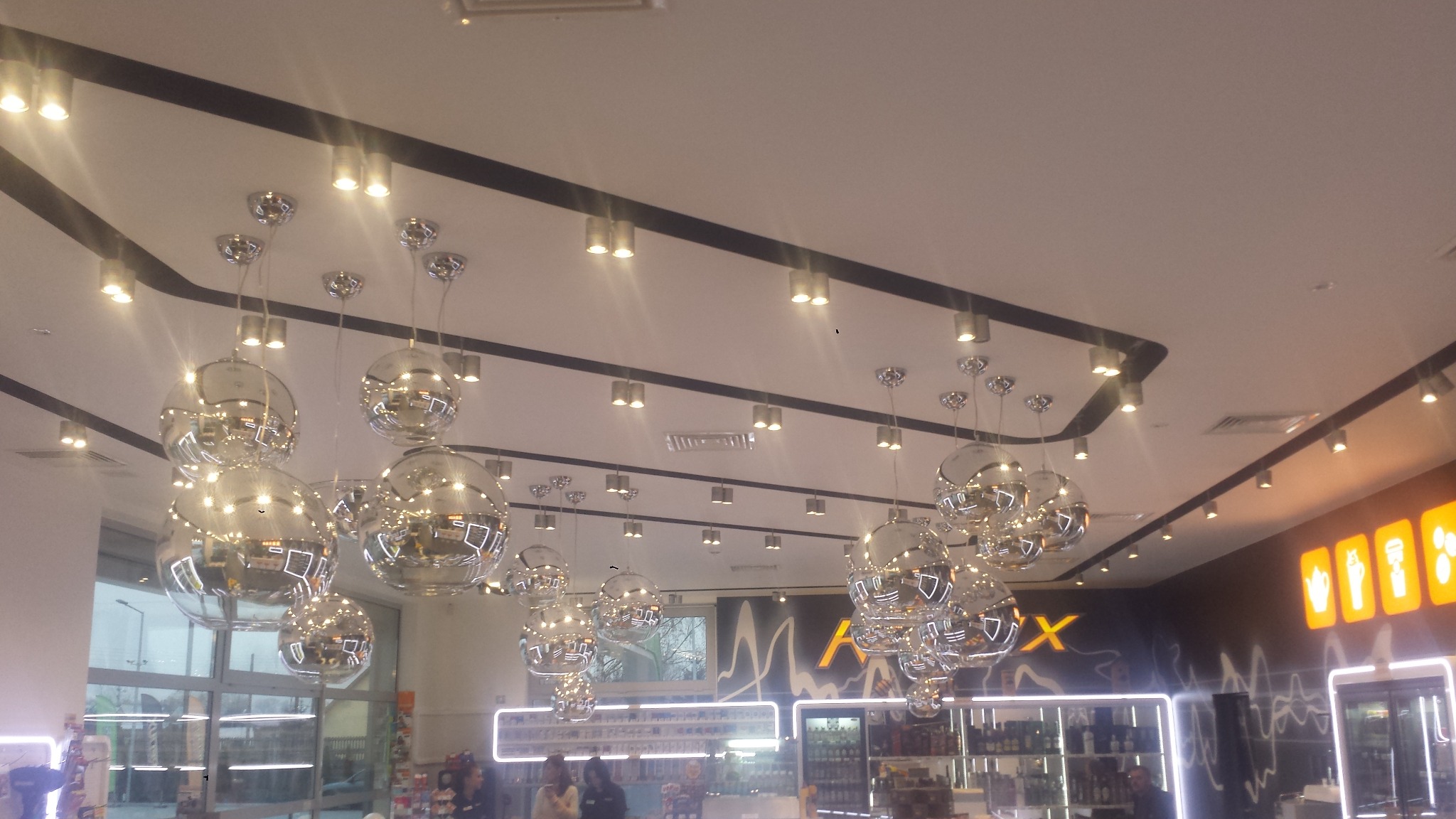Oświetlenie sufitowe z licznymi chromowanymi kulami-reflektorami zawieszonymi na cienkich linkach, w tle widoczne oświetlenie liniowe i fragmenty wnętrza sklepu.