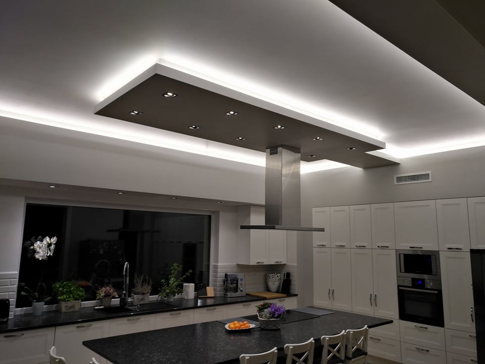 Nowoczesna kuchnia z wyspą i podwieszanym sufitem z oświetleniem LED, widok na okno i zabudowę kuchenną w stylu klasycznym.