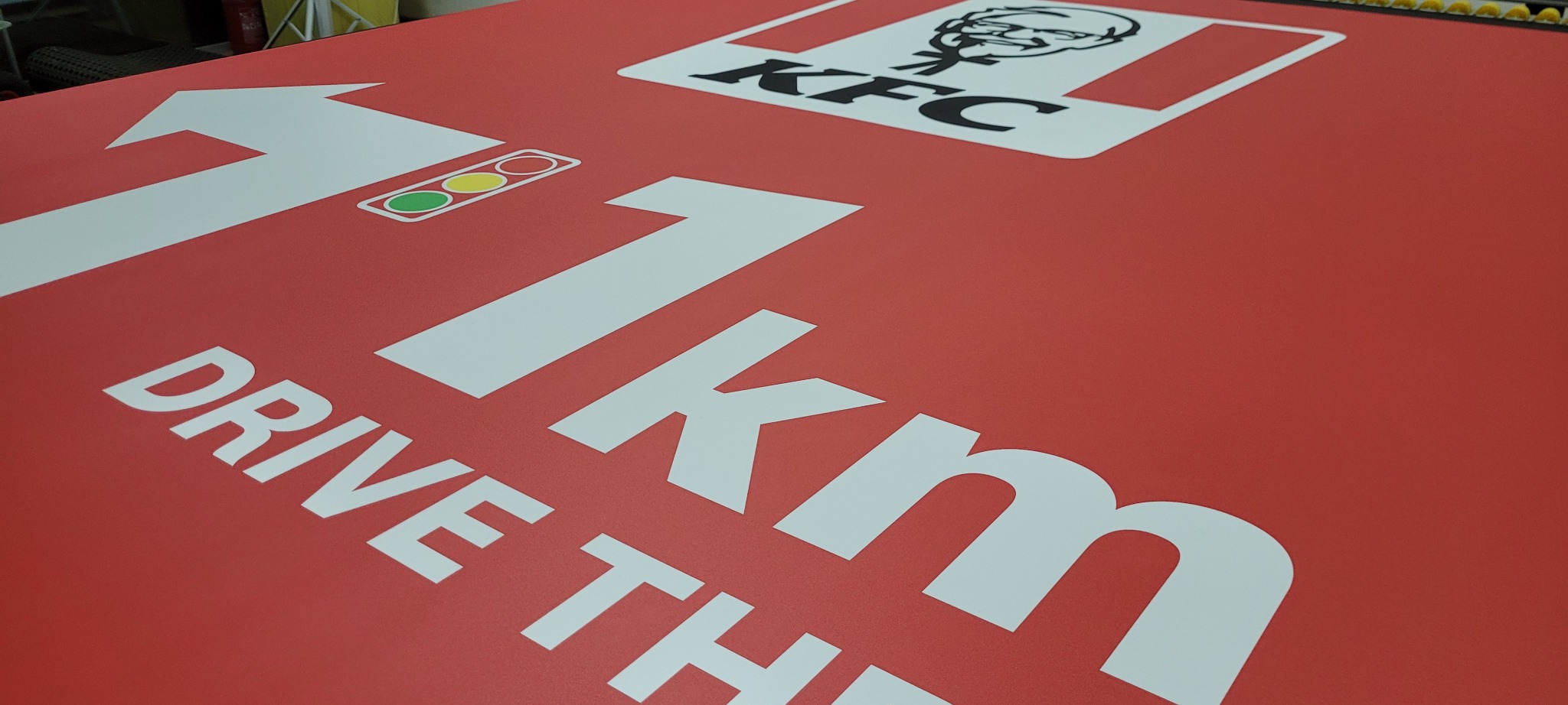Wydruk wielkoformatowy dla KFC w Krosno: czerwona tablica informacyjna z białym napisem '1.1 km DRIVE THRU' i strzałką, sygnalizująca odległość do restauracji.