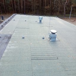 ASVOLT USŁUGI ELEKTRYCZNE ADRIAN SZCZĘCH - Płaski dach pokryty papą z zamontowanymi odgromnikami i wentylatorami, na tle lasu.