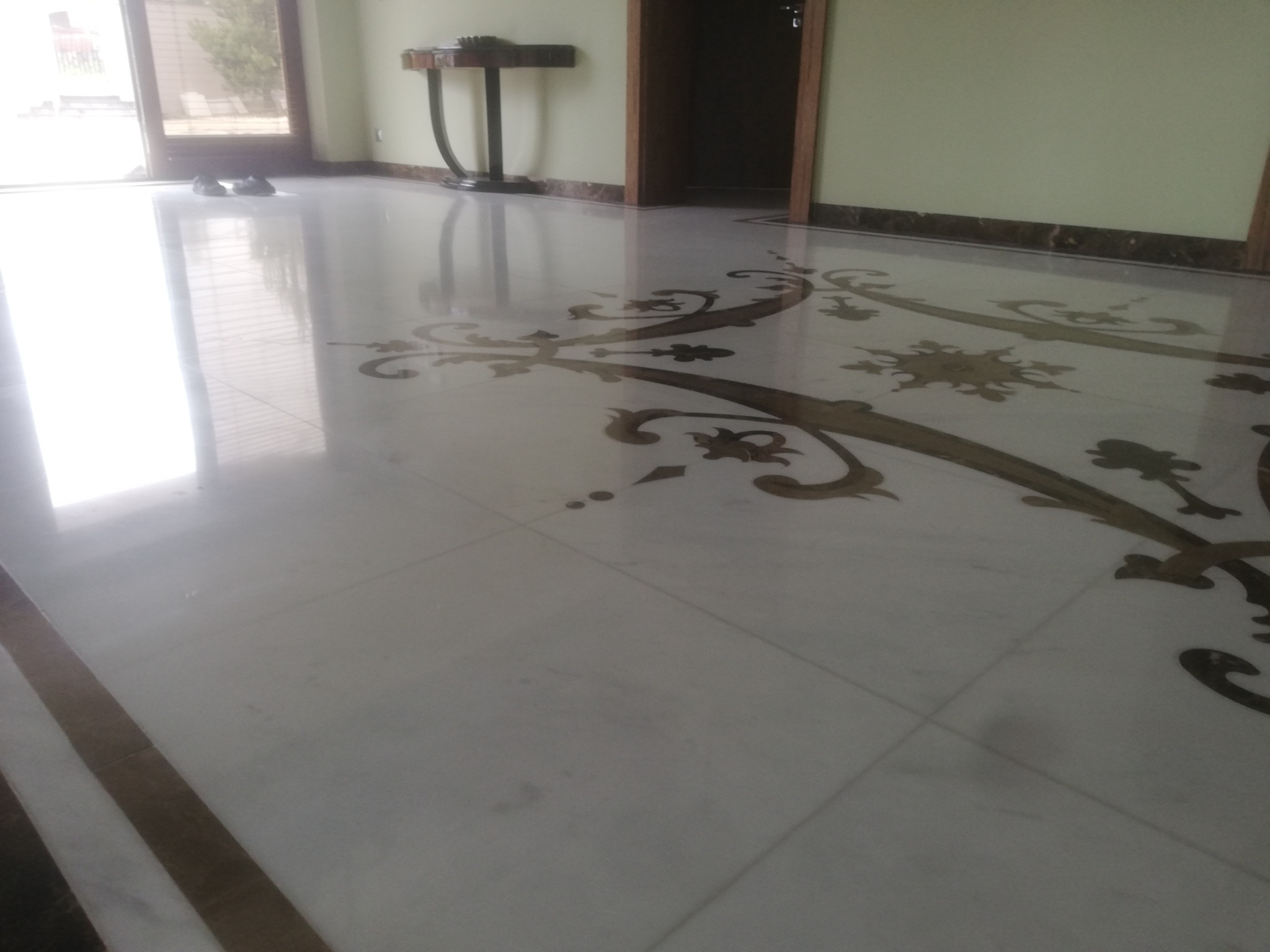 Błyszcząca marmurowa podłoga z dekoracyjnymi intarsjami w odcieniach brązu w przestronnym wnętrzu.