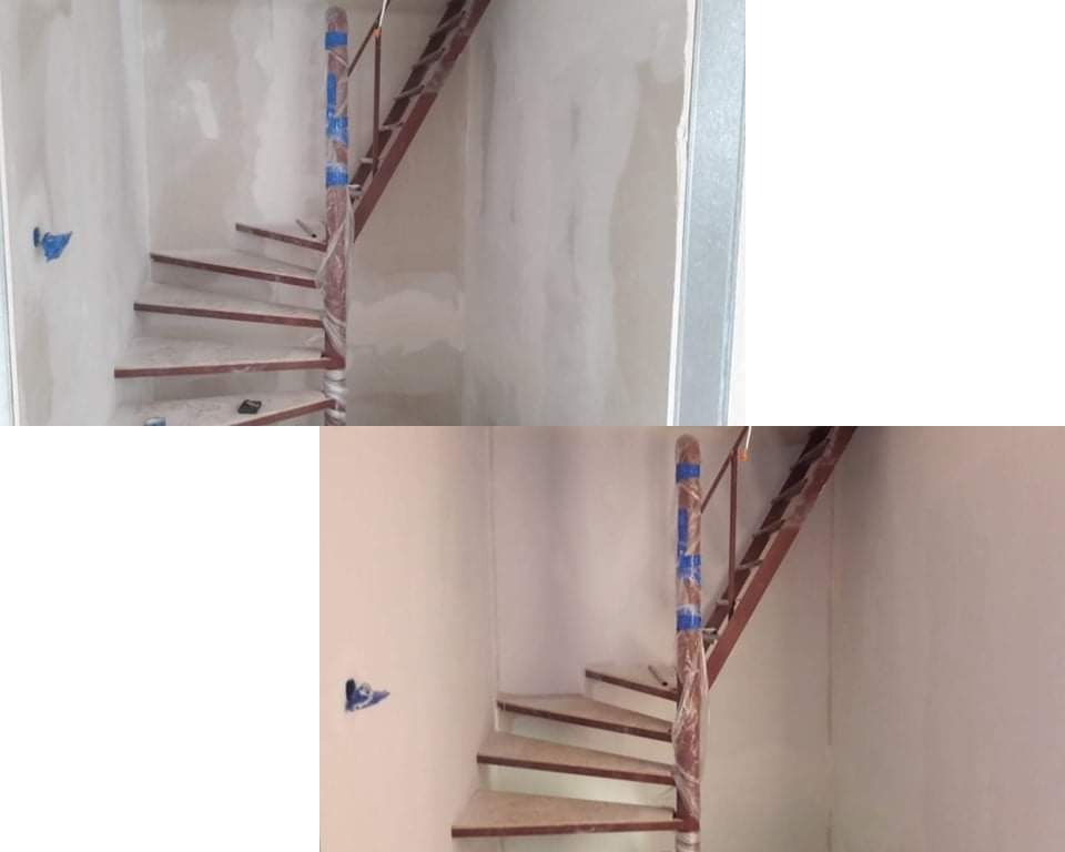 Wnętrze w trakcie prac: schody spiralne z drewnianymi stopniami, zabezpieczona folią kolumna centralna, surowe ściany przed malowaniem, widoczne ślady szpachlowania.