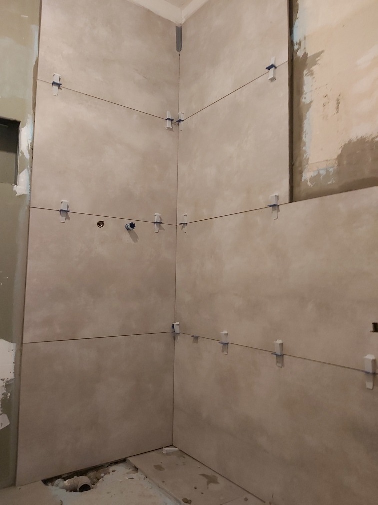 Montaż beżowych płytek w łazience, widoczne krzyżyki dystansowe i poziomica laserowa, surowy stan przed fugowaniem.