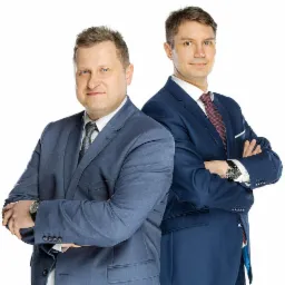 Portret dwóch pewnych siebie prawników w garniturach, stojących na białym tle z założonymi rękami i uśmiechem.