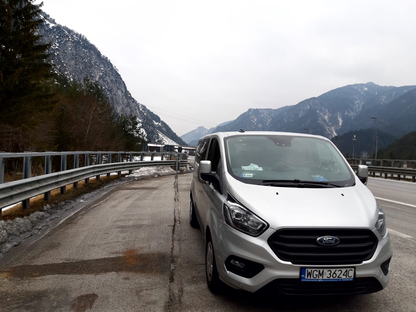Srebrny Ford Transit na poboczu drogi z widokiem na ośnieżone góry w tle.