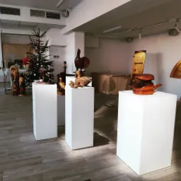 Wnętrze galerii z drewnianymi rzeźbami zwierząt na białych postumentach, w tle choinka i inne elementy wystroju.