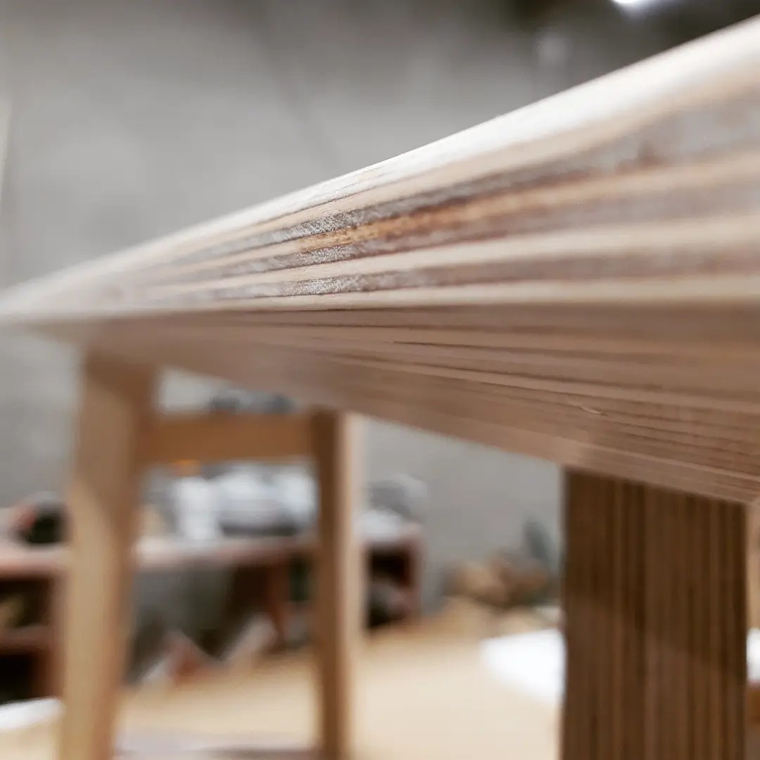 Fragment konstrukcji drewnianej z widocznymi warstwami sklejki, prawdopodobnie w trakcie montażu, z rozmytym tłem warsztatowym.