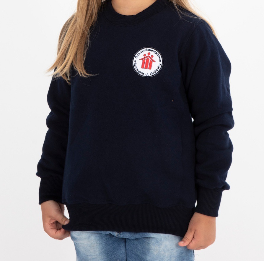 Dziewczynka w granatowej bluzie dresowej z naszytym logo Szkoły Salezjańskiej w Szczecinie, widoczne fragmenty jeansów.