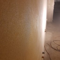 DR TYNK Dawid Radtke - Świeżo nałożona, strukturalna warstwa tynku w odcieniach beżu, widoczna z bliska na ścianie w Rumi, z wystającymi puszkami elektrycznymi i zwisającym przewodem na podłodze.