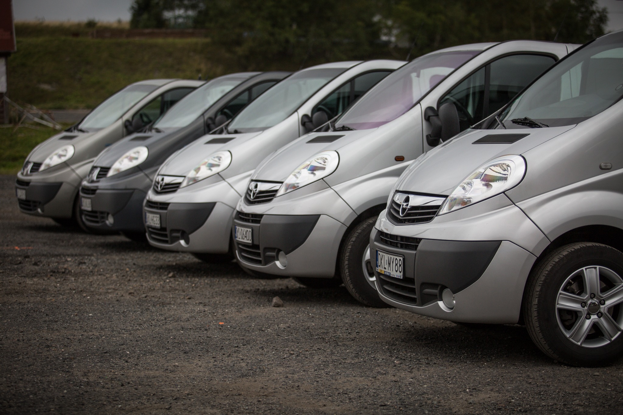 Szereg srebrnych vanów Opel Vivaro zaparkowanych w Wałbrzychu, widok z przodu, z widocznymi tablicami rejestracyjnymi i oponami, sugerujący flotę pojazdów.