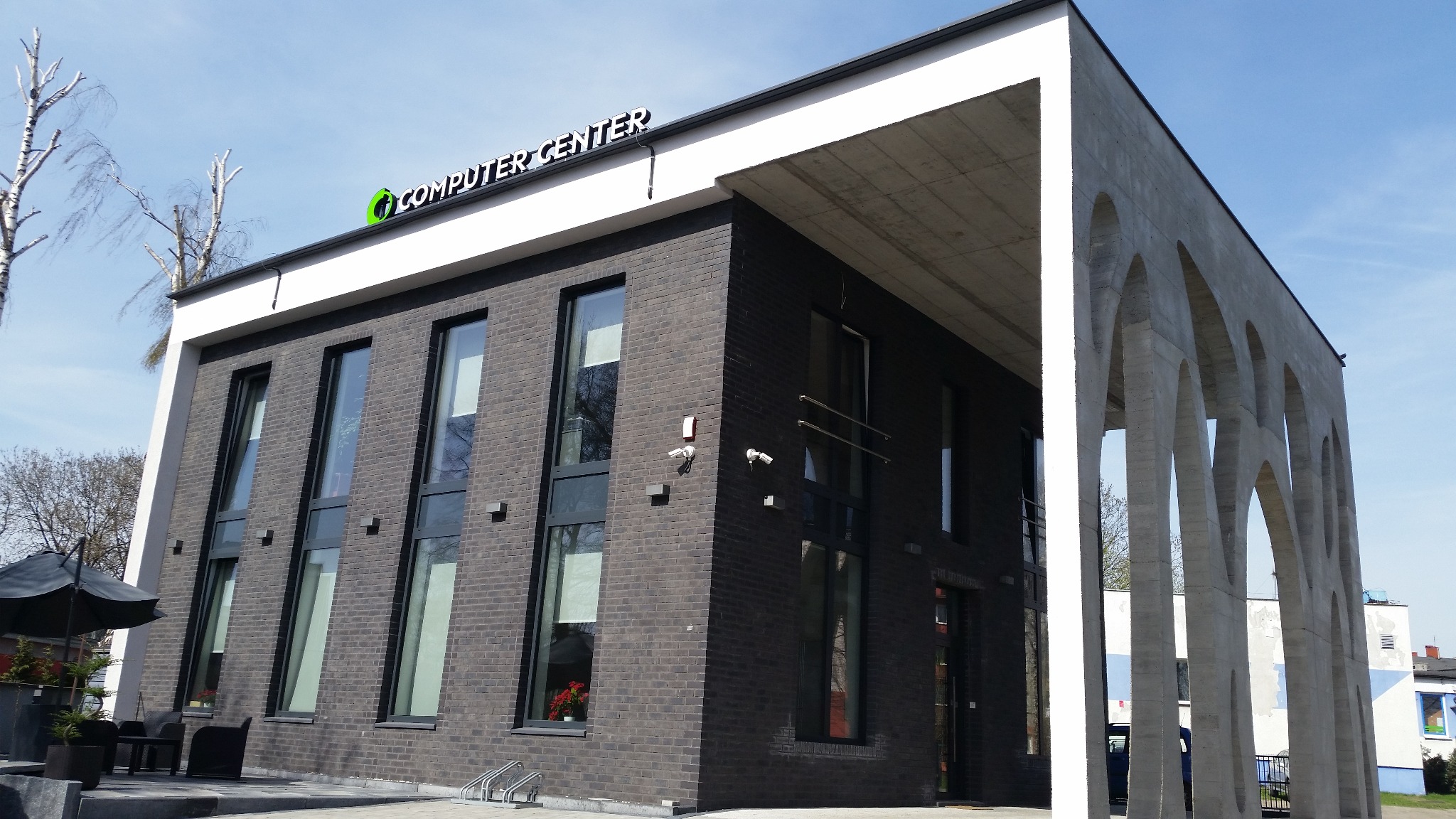 Budynek Computer Center z czarnej cegły z białymi elementami architektonicznymi, widoczne kamery monitoringu i logo firmy na dachu.