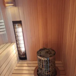 Wnętrze sauny z drewnianymi panelami, piecem Harvia wypełnionym kamieniami i grzejnikiem na ścianie.