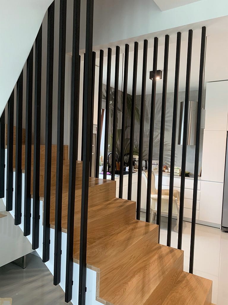 Schody drewniane z czarną, pionową balustradą, widok na nowoczesną kuchnię z tapetą w tropikalne liście