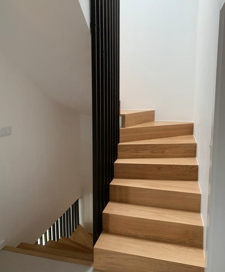 Nowoczesne schody drewniane z czarną, pionową balustradą, minimalistyczny design, jasne wnętrze, widok z dołu.