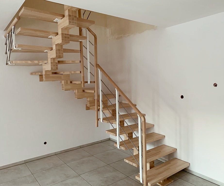 Drewniane schody ażurowe z metalową balustradą w jasnym wnętrzu, widoczne mocowania stopni do ściany.