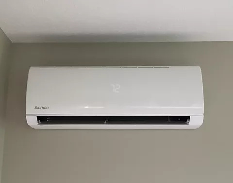 Biała klimatyzacja ścienna marki Chigo z wyświetlaczem temperatury ustawionym na 72, zamontowana na szarej ścianie w biurze.