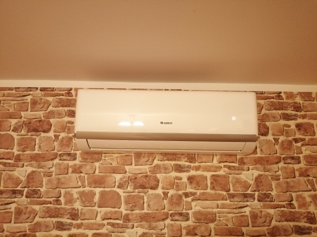 Biała jednostka klimatyzacji marki Gree zamontowana na ścianie z dekoracyjną okładziną imitującą kamień w Jaworznie.