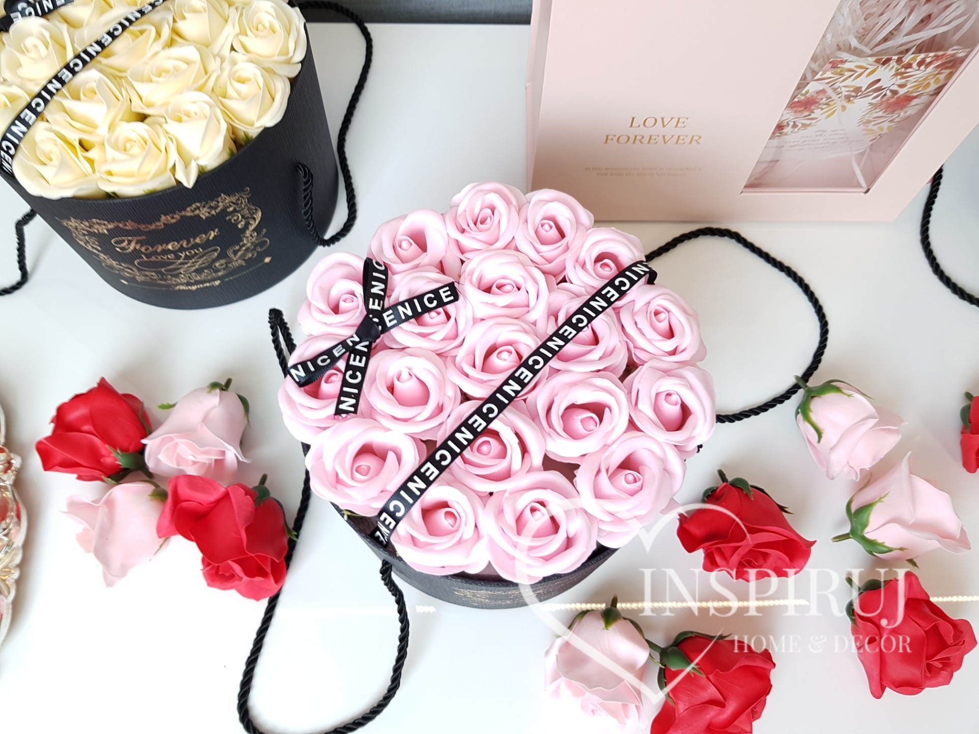 Różowe i kremowe róże z mydła w czarnych pudełkach z napisem 'Forever Love You' i wstążką 'NICENICENICENICE', kilka pojedynczych czerwonych i różowych róż obok.