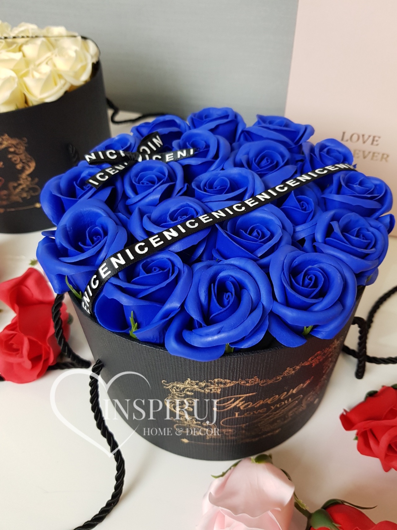 Kompozycja z intensywnie niebieskich, sztucznych róż w czarnym, okrągłym pudełku z napisem 'Forever Love You', przewiązana wstążką z napisem 'NICE NICE NICE'.