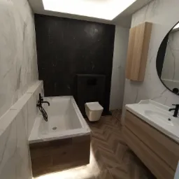 Nowoczesna łazienka z marmurowymi płytkami, czarną ścianą, podświetlaną wanną i drewnianymi akcentami, widok na umywalkę z okrągłym lustrem.