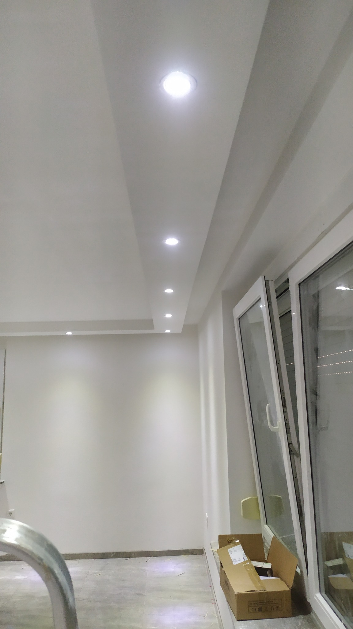 Równomiernie rozmieszczone, okrągłe lampy sufitowe LED w nowym, jasnym pomieszczeniu z otwartym oknem i kartonami na podłodze.