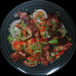 Kompozycja z grillowanej wieprzowiny, czerwonej papryki, cebuli i zielonej pietruszki, podana w ciemnym, okrągłym naczyniu.