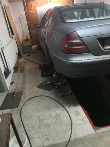 Szary samochód na podnośniku w warsztacie, z otwartą maską i widocznymi narzędziami obok kanału inspekcyjnego.