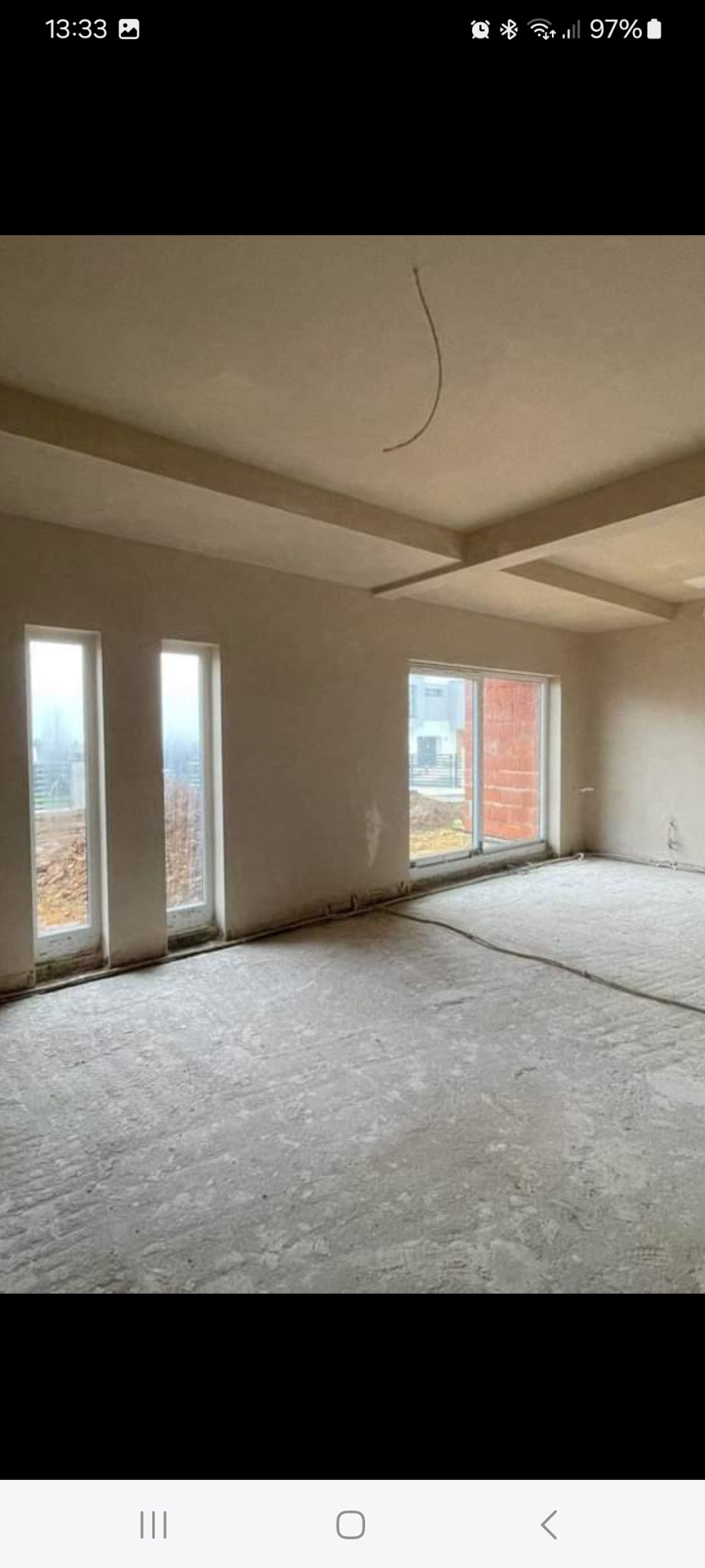 Wnętrze pokoju po nałożeniu tynków, z widocznymi oknami i surowym wykończeniem podłogi. Widoczne elementy instalacji elektrycznej.