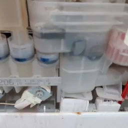 Wnętrze zmywarki w trakcie naprawy w Krakowie, widoczne elementy układu doprowadzania wody i dozowania detergentu, z numerami seryjnymi i datami produkcji na plastikowych komponentach.