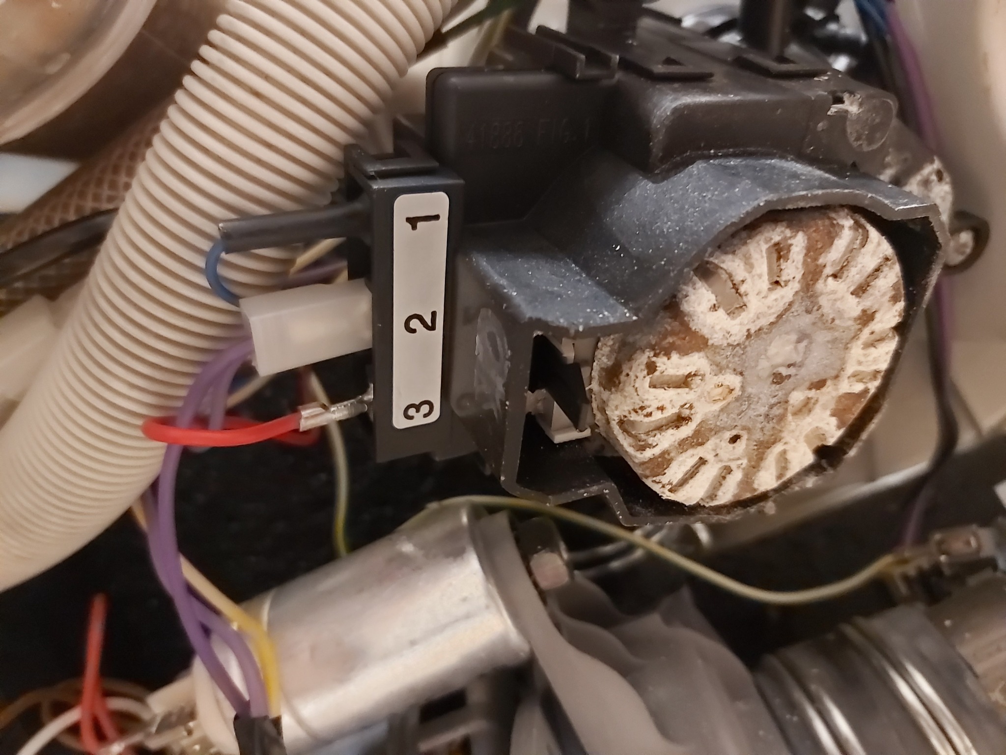 Zdemontowany moduł pompy obiegowej z widocznym zakamienieniem na wirniku, przewody elektryczne podłączone do listwy z numerami 1, 2, 3, w tle karbowana rura dopływowa.