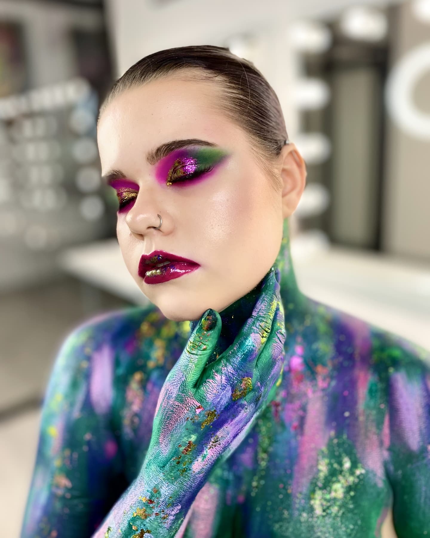 Portret kobiety z artystycznym, wielokolorowym makijażem oczu w odcieniach fioletu, zieleni i złota, z błyszczącymi ustami w kolorze burgundu i ciałem pomalowanym w abstrakcyjne wzory w odcieniach...