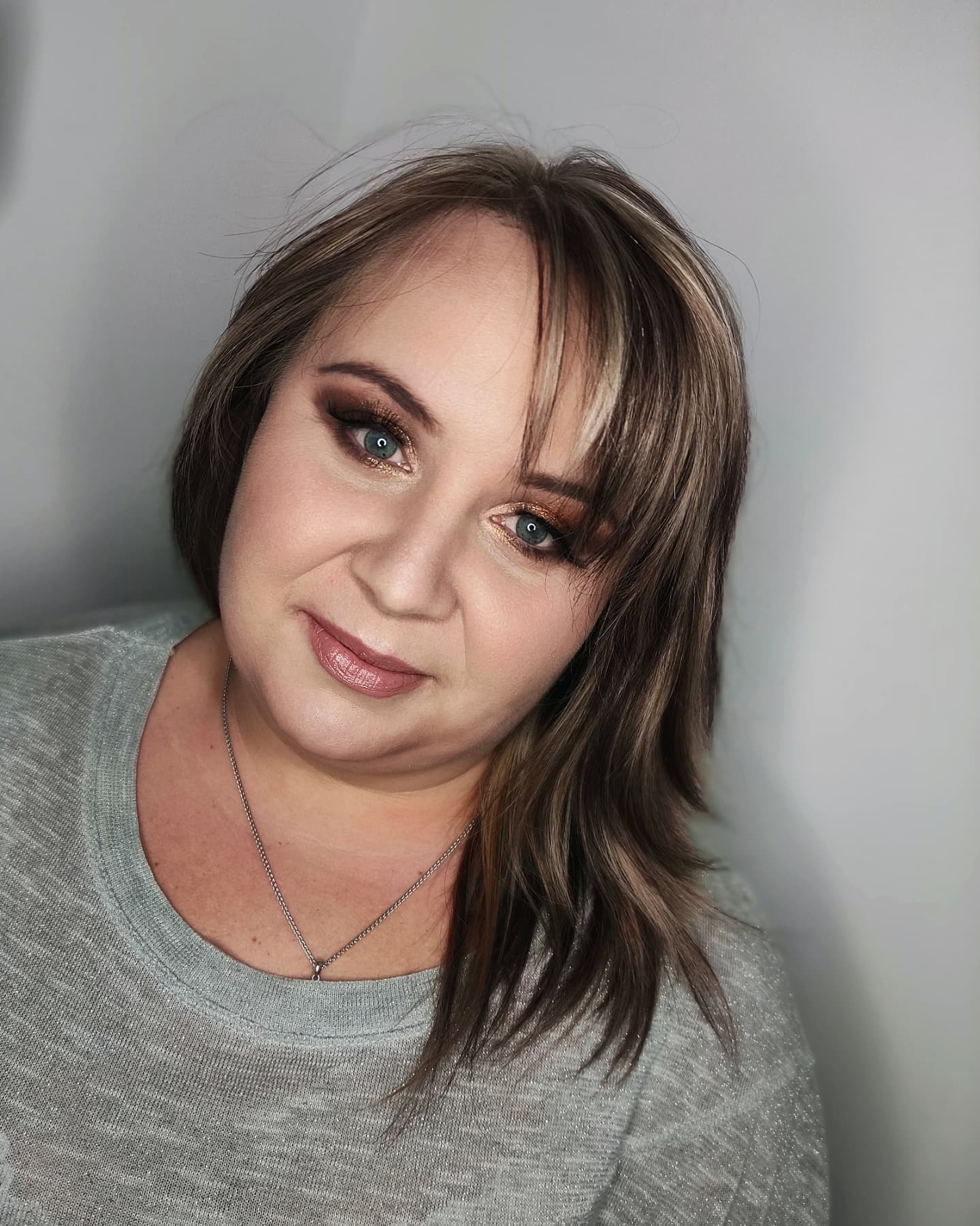 Portret kobiety z brązowym makijażem oczu, beżową szminką i blond pasemkami we włosach, patrzącej w obiektyw.