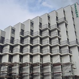 Przembud Przemysław Tokarzewski - Nowoczesna, biała elewacja budynku Rosomak z kaskadowymi balkonami i czarnymi balustradami, częściowo z rusztowaniami i pracownikiem.