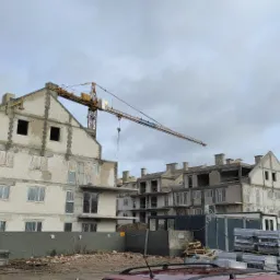 Wznoszenie budynku wielorodzinnego z betonu komórkowego, widoczny żuraw budowlany i materiały budowlane na placu budowy.