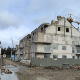 PARBAT Sp.z o. o. - Wznoszenie budynku wielorodzinnego z betonu komórkowego w Warszawie, widoczny żuraw wieżowy i materiały budowlane składowane na terenie budowy, po deszczu.