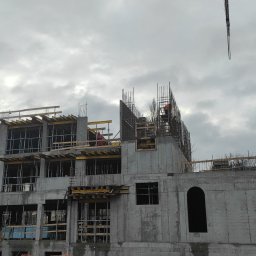 PARBAT Sp.z o. o. - Wznoszenie wielopiętrowego budynku w konstrukcji żelbetowej z widocznym żurawiem, szalunkami i zbrojeniami na tle pochmurnego nieba.