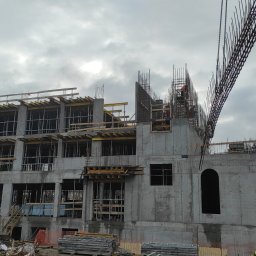 PARBAT Sp.z o. o. - Wznoszenie wielopiętrowego budynku żelbetowego: szkielet konstrukcji z widocznym zbrojeniem, deskowaniem i dźwigiem w pochmurny dzień.