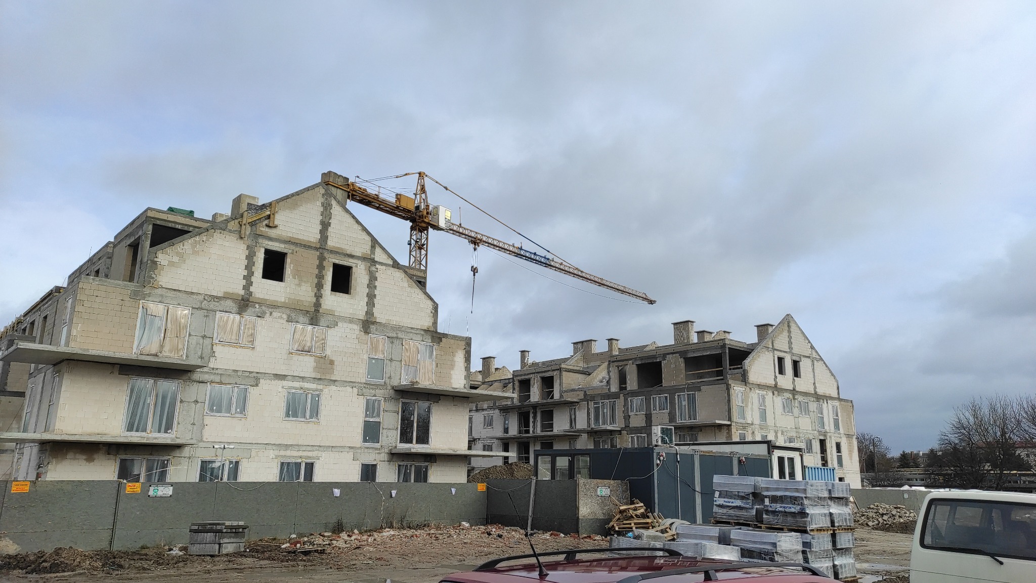 Wznoszenie budynku wielorodzinnego z betonu komórkowego, widoczny żuraw budowlany i materiały budowlane na placu budowy.