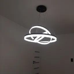 Nowoczesny, trójkołowy, ledowy żyrandol z czarną rozetą sufitową, zamontowany w jasnym pomieszczeniu z białą ścianą i drzwiami.