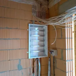 Rozprowadzenie przewodów elektrycznych w peszlach, w nowym budynku z pustaków ceramicznych, z białą skrzynką rozdzielczą w trakcie montażu.