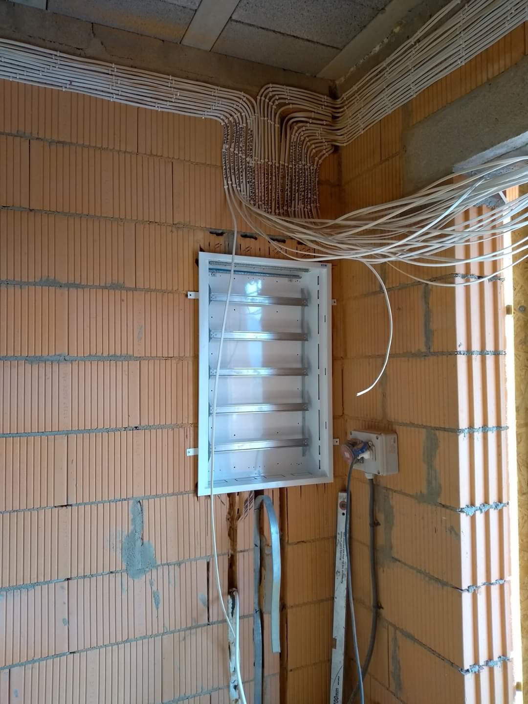 Rozprowadzenie przewodów elektrycznych w peszlach, w nowym budynku z pustaków ceramicznych, z białą skrzynką rozdzielczą w trakcie montażu.