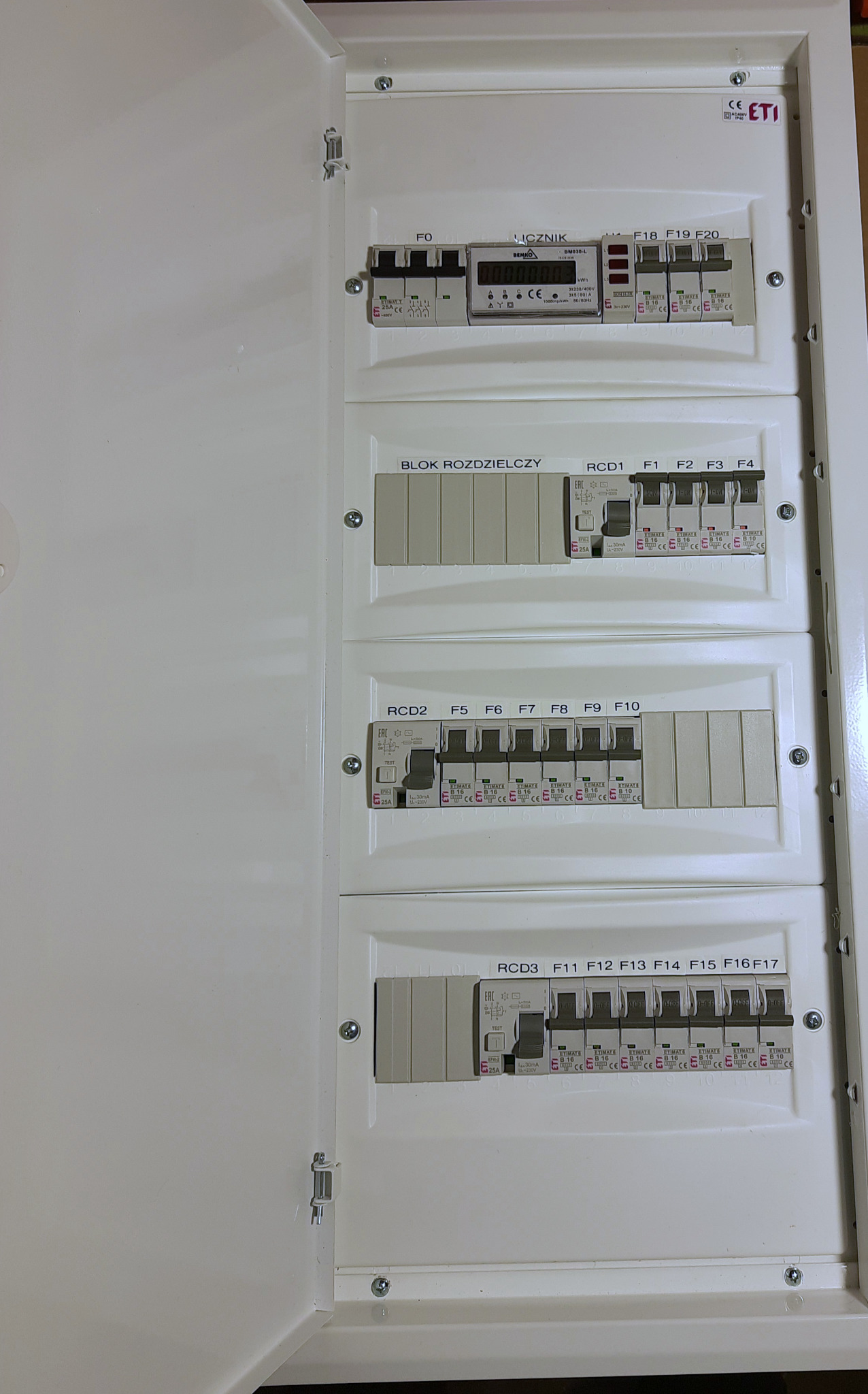 Otwarta skrzynka rozdzielcza z zamontowanymi bezpiecznikami ETI, licznikiem energii i blokami rozdzielczymi, widok z bliska.