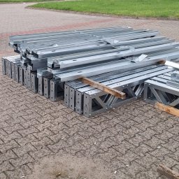 easybox sp. z o.o. - Stalowe, ocynkowane elementy konstrukcyjne domu szkieletowego ułożone na betonowej kostce brukowej, widoczne otwory montażowe i wzmocnienia poprzeczne.