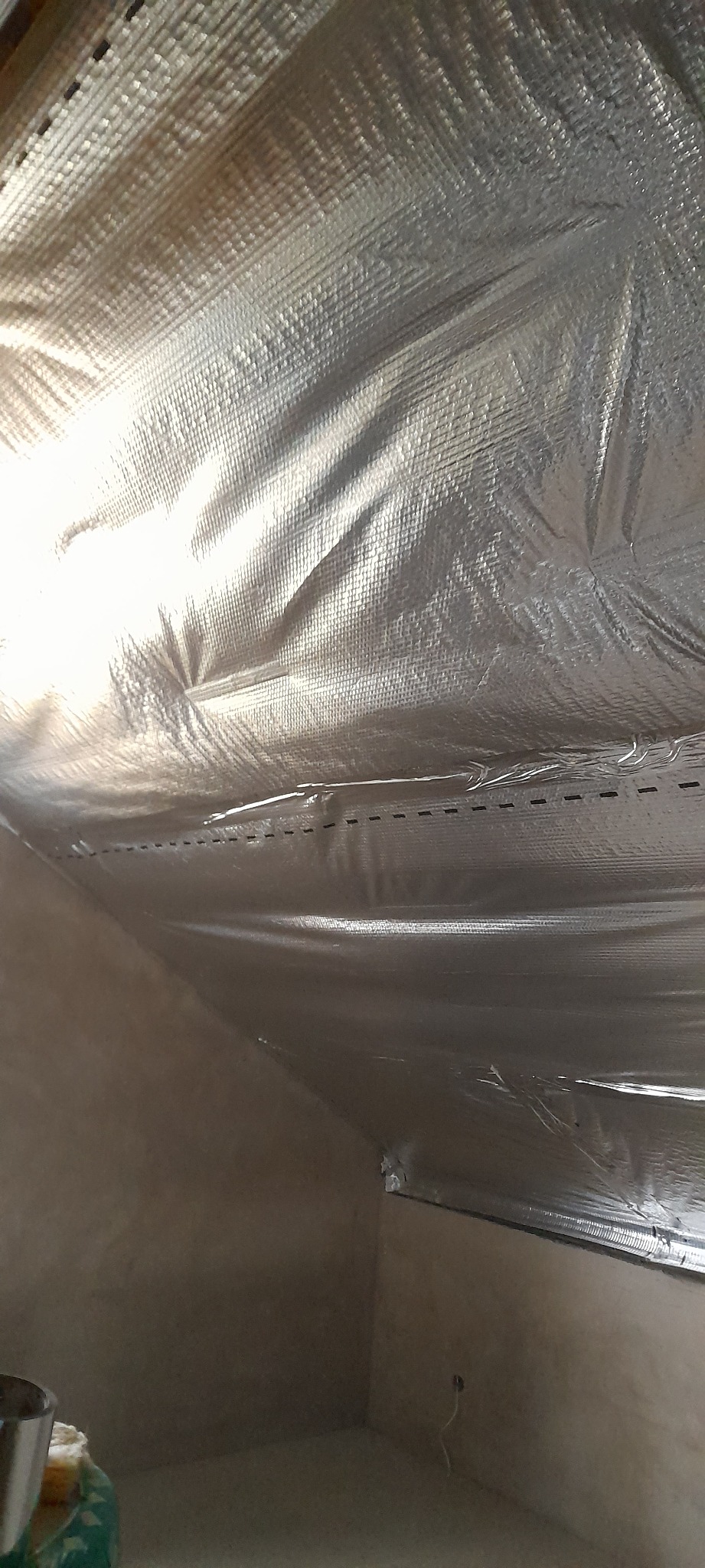 Wnętrze poddasza z widoczną folią termoizolacyjną przymocowaną do krokwi za pomocą zszywek, przygotowane do dalszych prac wykończeniowych.