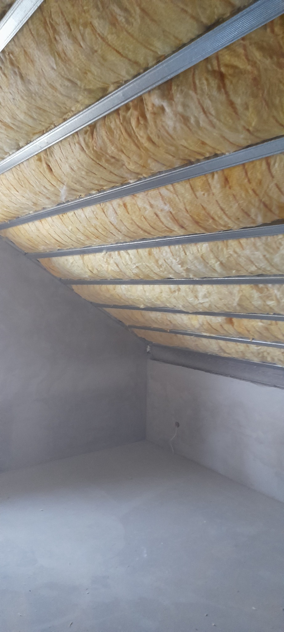 Poddasze w trakcie prac: widoczne ocieplenie z wełny mineralnej zamontowane między profilami metalowymi sufitu podwieszanego, ściany w stanie surowym.