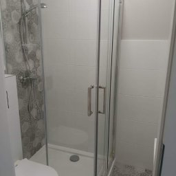Emilian Fedorowicz Usługi remontowo budowlane - Nowoczesna kabina prysznicowa z chromowanymi profilami i szklanymi drzwiami, widoczna toaleta i płytki w geometryczne wzory na ścianie prysznica i podłodze.