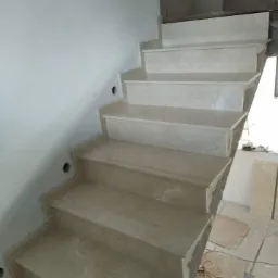 Wewnętrzne schody wykończone jasnym kamieniem, widoczne otwory na oświetlenie w ścianie, częściowo ukończony montaż.