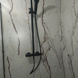 Czarny zestaw natryskowy zamontowany na ścianie wyłożonej płytkami imitującymi marmur z wyraźnym, brązowym żyłowaniem.