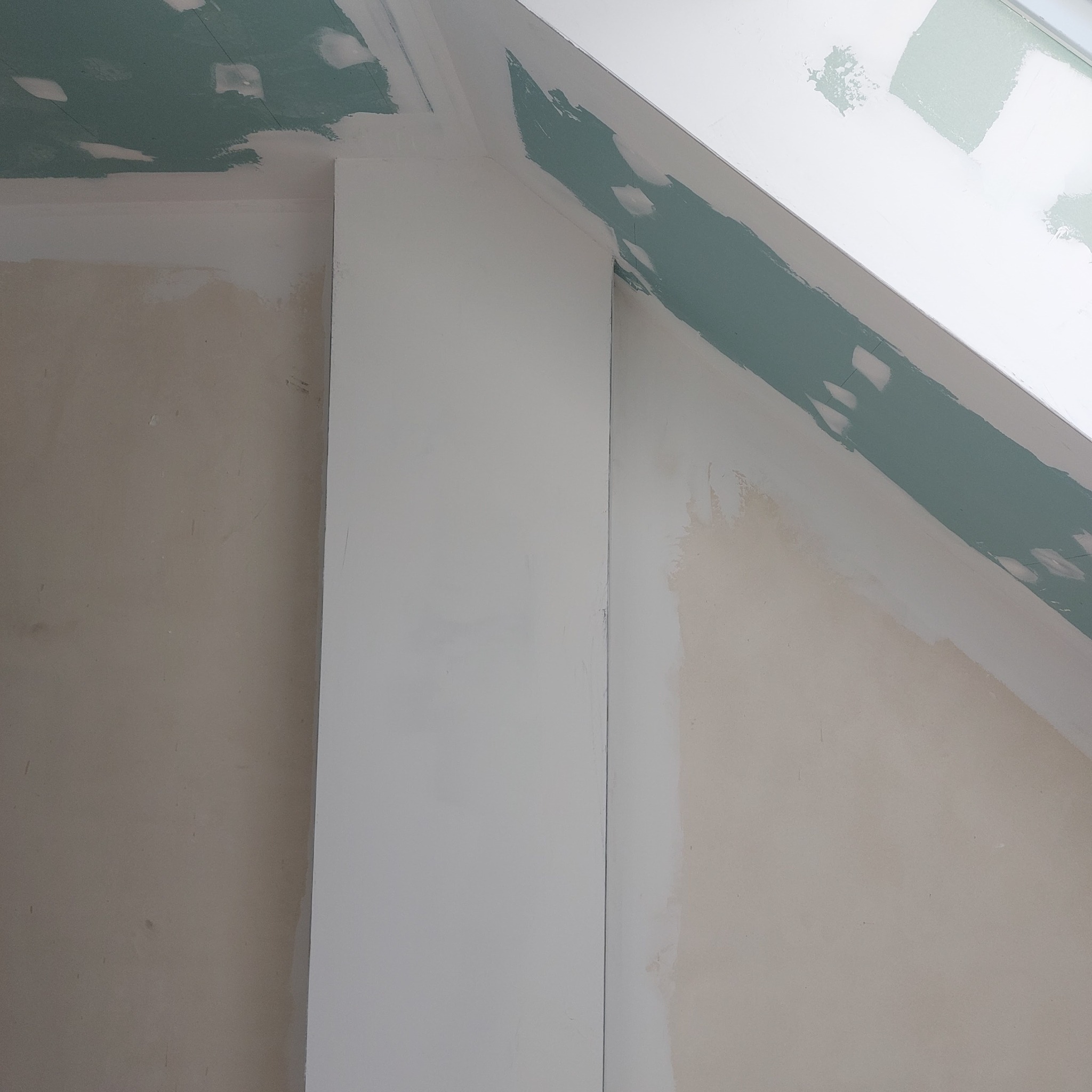 Ściana pod skosem w trakcie wykańczania: zielona szpachla maskuje łączenia płyt karton gips na suficie, gładź na ścianach, biała kolumna.